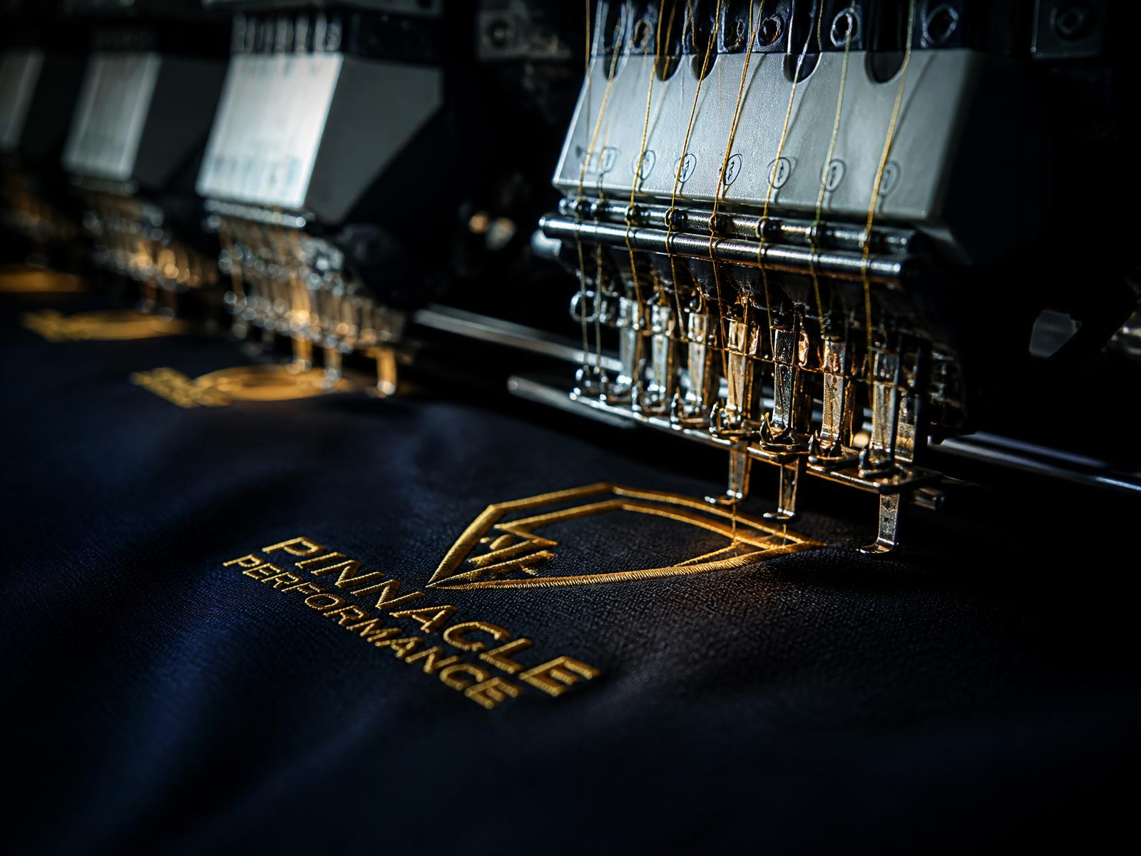 Máquina industrial de bordado trabajando un logotipo con hilo dorado